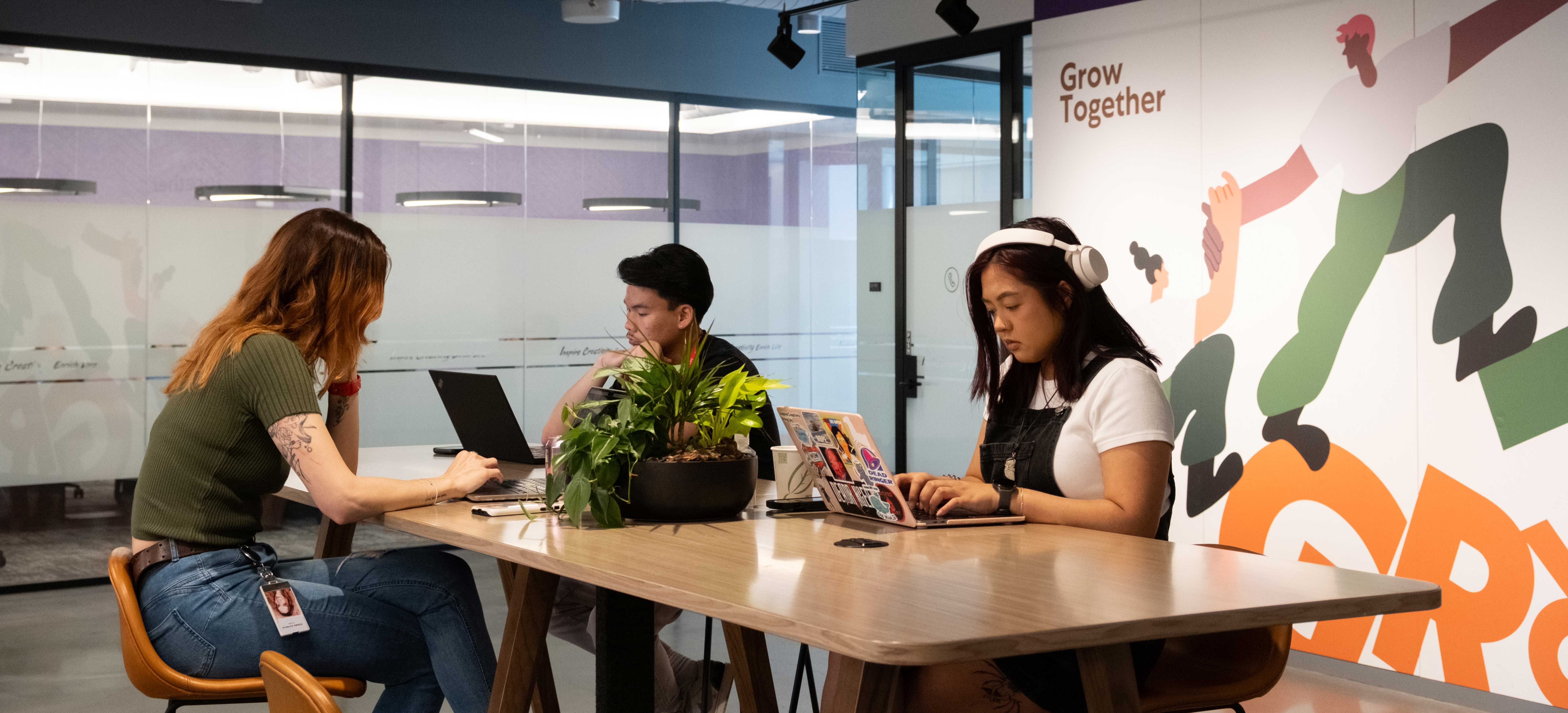 A male and a female TikTok employee talk and smile as they sit beside each other and work on a project together.